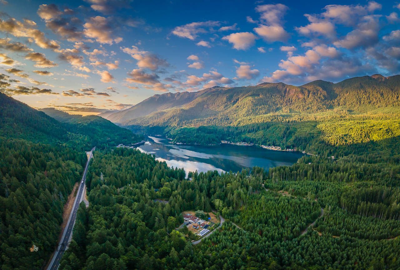 Pillow clouds over a mountain lake at sunrise, surrounded by forest with a two-lane road